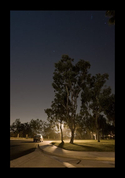 street at night with parked car, trees and distant stars